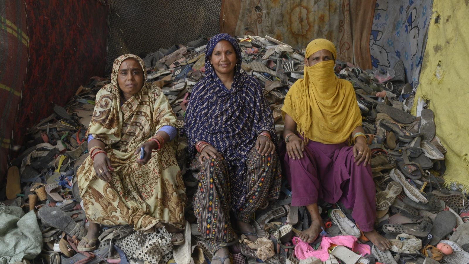 Three women waste segregators sit among a pile of discarded footwear at the Bhalswa landfill, New Delhi.